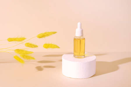 White round podium with cosmetic bottle on beige pastel background and yellow dried flowers with shadows for product presentation. Front view. Copy space.の写真素材
