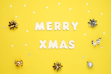 Balls, glitter stars, gift box, gray decorations on yellow background and the words Merry xmas made of wooden letters. Christmas, New Year concept. Top view.の写真素材