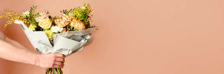 Man holding and giving a beautiful bouquet with flowers to woman on beige background. Front view. Valentines, womens, mothers day, love concept. Bannerの写真素材