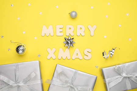 Balls, glitter stars, gift box, gray decorations on yellow background and the words Merry xmas made of wooden letters.の写真素材