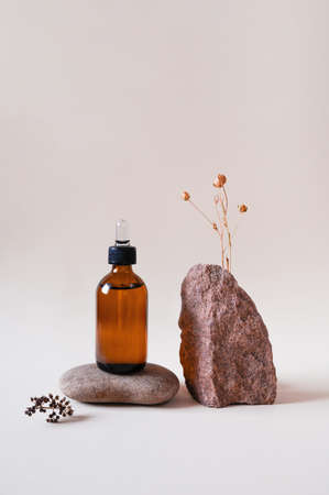 Cosmetic in a glass bottle on stone podium, dried flower on beige background. Front view.の写真素材