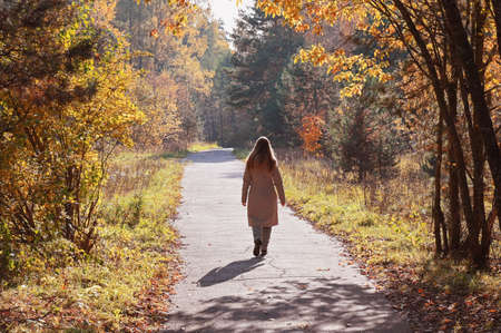 A young woman walking in the autumn park. Hello october. Beautiful trees with dried colourful leavesの写真素材