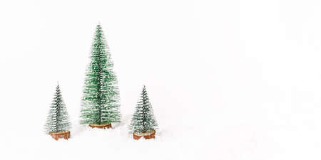 Miniature christmas trees on background with white snow. New year concept. Copy space, front view. Banner.の写真素材