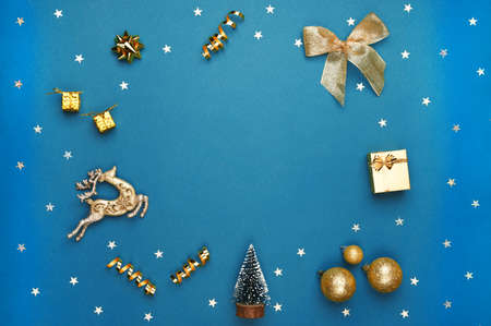 Christmas composition with bow, balls, toys, glitter, golden decor on blue background. Flat lay, top view. Copy spaceの写真素材