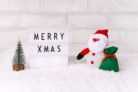 Santa Claus doll toy with miniature fir tree and gift bag on christmas time, background with snow. Front viewの写真素材