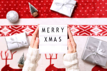 Close-up of lightbox with text merry christmas in hands and background with christmas gifts, miniature trees. Top viewの写真素材