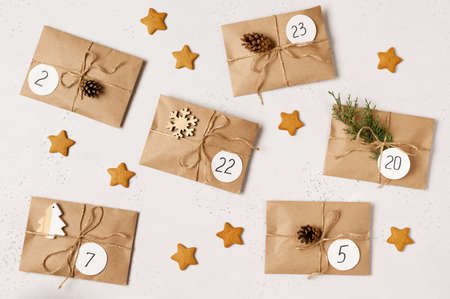 Christmas advent calendar. Flat lay with kraft envelopes with gifts, fir branches, pine cones, ginger biscuits. Top view.の写真素材