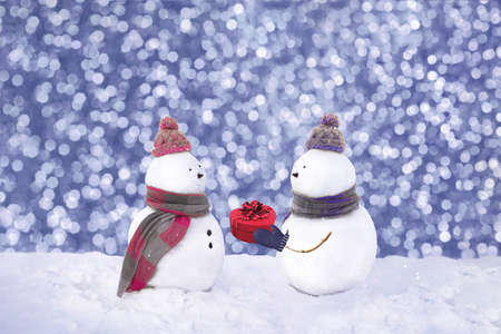 Snowmen in love wearing winter hats, scarves on a white background. Boy giving a gift to his girlfriend. Christmas, Valentins day, love concept. 14th february. Copy space. Trendy color of the year 2022. Very peri.の写真素材