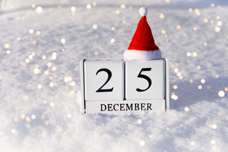 Christmas cocept. December 25 calendar numbers and Santa hat on snow background with lights.の写真素材