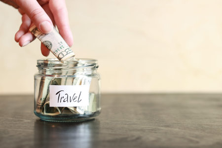 Piggy bank with dollars for travel. Glass jar with money. The woman puts more money in the piggy bank.