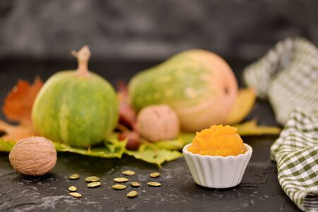 Fresh homemade vegan pumpkin puree or mash in small bowl, among autumn attributes:walnut, yellow leaves, pumpkin and pumpkins seedsの写真素材
