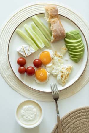 Healthy breakfast with eggs, avocado, cucumber and toast on a white backgroundの写真素材
