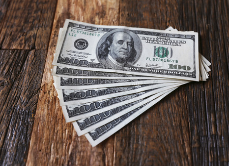Amount of dollars are lying on the wooden brown table. Dollars are located in fan position.の写真素材