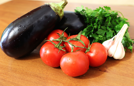 Tasty seasonal vegatables: eggplants, tomatos, garlic, parsley are on the tableの写真素材