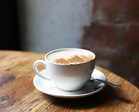 Cup of tasty latte is standing on the wooden textured table with the brick wall background.  Latte is in the white big cup.の写真素材