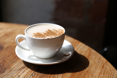 Cup of tasty latte is standing on the wooden textured table with the brick wall background.  Latte is in the white big cup.の写真素材