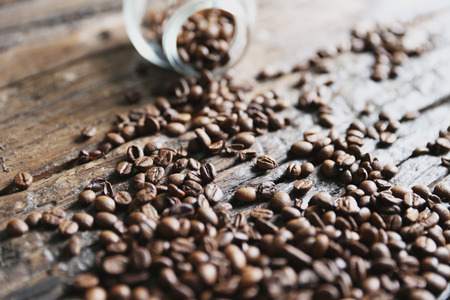 Coffee beans are on the wooden textured table with the glass jarの写真素材