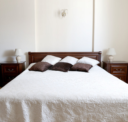 Big light bedroom in the home. Bed is decorated by brown and beige colors pillows.の写真素材