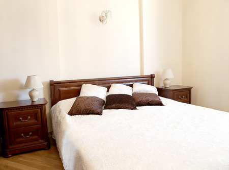 Big light bedroom in the home. Bed is decorated by brown and beige colors pillows.の写真素材