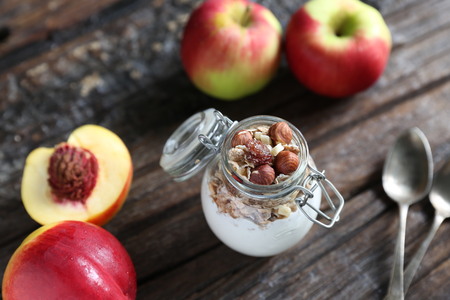 Glass jar with yogurt, granolla and almond nuts in it. Nectarin and apples are on the wooden backgound with spoons closed to the jar.の写真素材