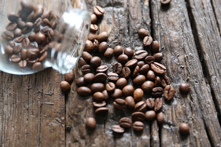 Coffee beans are on the wooden textured table with the glass jarの写真素材