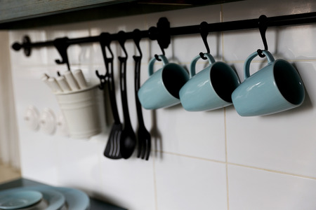 blue cups is located on the pure white wall in the kitchen above the owen. closed to cups are located some other applience needed for cookingの写真素材
