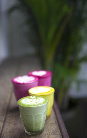 Beetroot, matcha,turmeric lattes are on the wooden table with the palms on the background, Trendy healthy drinksの写真素材