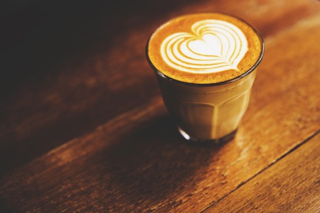 Cup of hot latte coffee is on the wooden table background