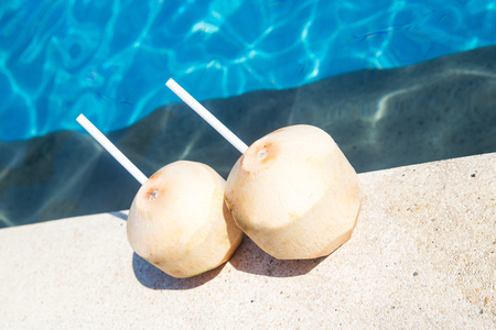 Two young fresh coconuts on edge of swimming pool. Tropical and summer moodの写真素材