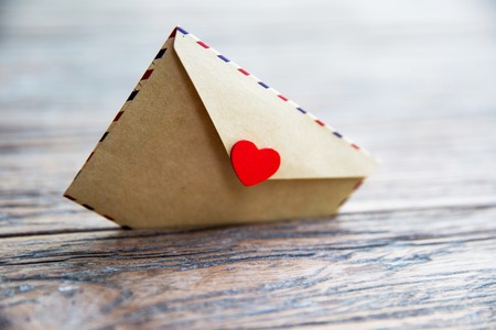 Craft small envelope with red heart sticks in the wooden textured background.の写真素材