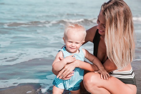 Young millennial mother is spending time with her cute baby boy on the beach.の写真素材