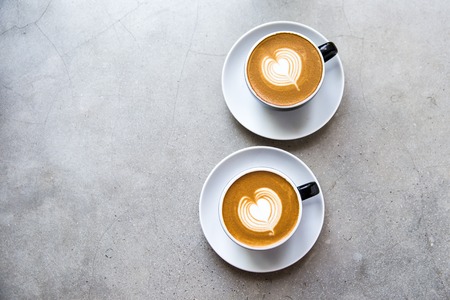 Two black cups of tasty cappucino with love art latte.の写真素材