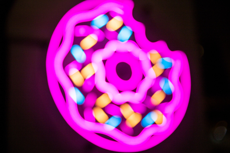 Donuts bright neon sign on cafe entrance on black background. Blurred motion. Trendy 80s.