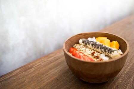 Mango smoothie bowl with strawberry, banana,coconut and oatmeal on wooden background.の写真素材