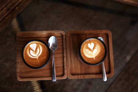 Two Cups of hot cappuccino on wooden desk with spoons on glass table background. Breakfast time. Top view.の写真素材