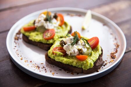 Smashed avocado toasts with cherry tomatoes and crumbled feta cheese on a plate on rye bread....