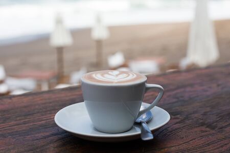 Cup of hot cappucino on wooden table background with ocean view background. Vacation concept.の写真素材