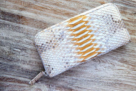 Light wallet from trendy snake python skin on wooden white background. Top view. Fashion concept.