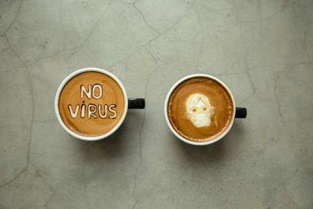 Two cup of Cappuccino with latte art: man in facial mask and sign No virus.