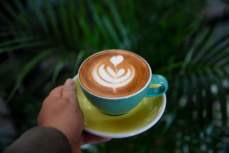 Woman holding green mug of cappuccino with latte art.