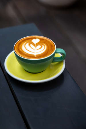 green mug of cappuccino with latte art on wooden background.の写真素材