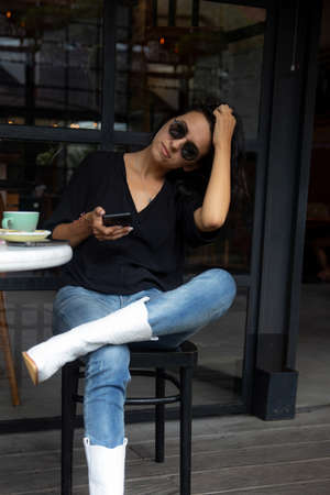 Image of beautiful stylish woman sitting on street stairs with legs crossed and holding mobile phoneの写真素材