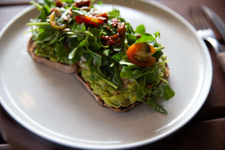 Healthy toast with avocado, arugula and sun dried tomatoes on rustic wooden table.の写真素材