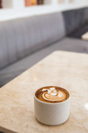 White cup of tasty cappuccino with latte art on white marble background in cafe, Loft interior,の写真素材
