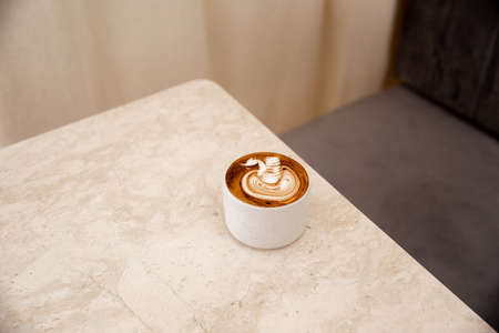 White cup of tasty cappuccino with latte art on white marble background in cafe, Loft interior,の写真素材