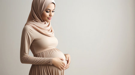 Hijab pregnant woman touching her belly on gray background with copy spaceの素材