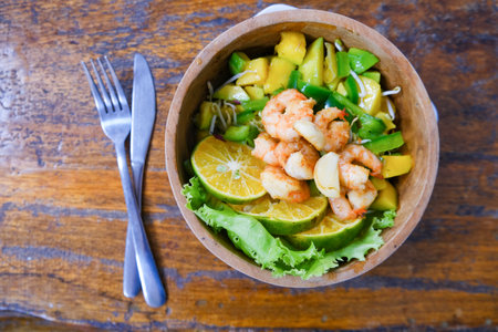 Fresh shrimp and mango salad with lime wedges served in a rustic wooden bowlの写真素材