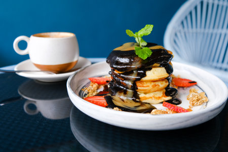stack of pancakes with chocolate syrup, caramel and strawberries and cup of coffee. Breakfast time at cafe, close upの写真素材
