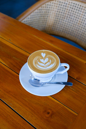 Latte Art on Cappuccino in White Cup at Wooden Cafe Tableの写真素材