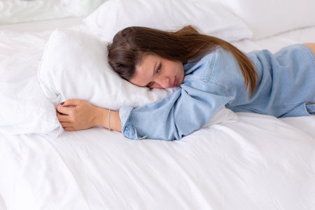 Serene Woman Relaxing on a White Bed in Casual Denim Shirtの写真素材
